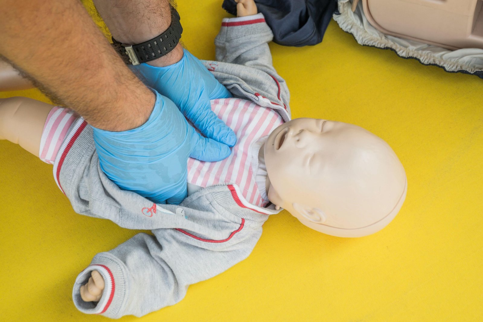 Hands performing CPR on an infant mannequin for a first aid training session.